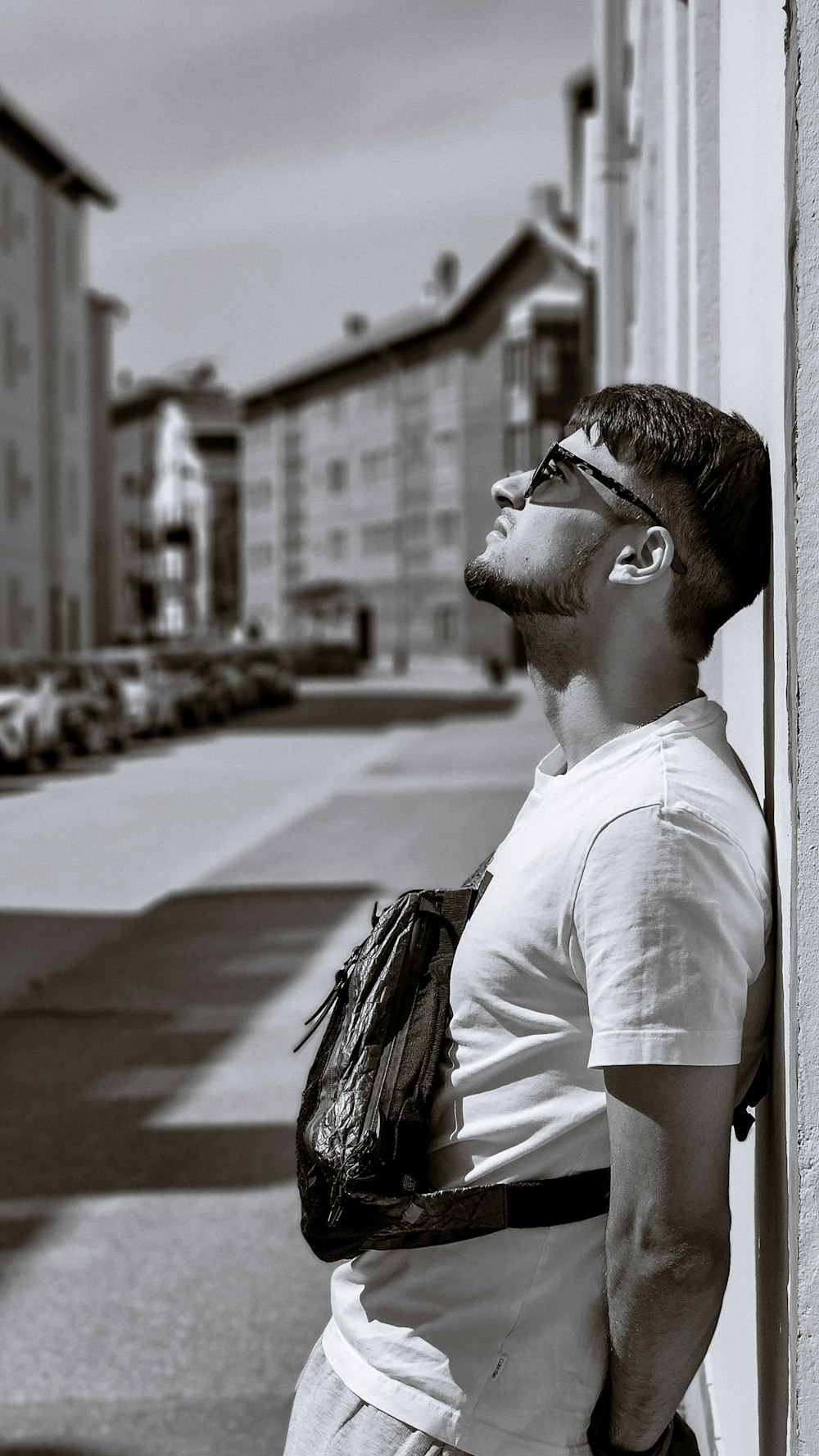 a man leaning against a wall with a bag