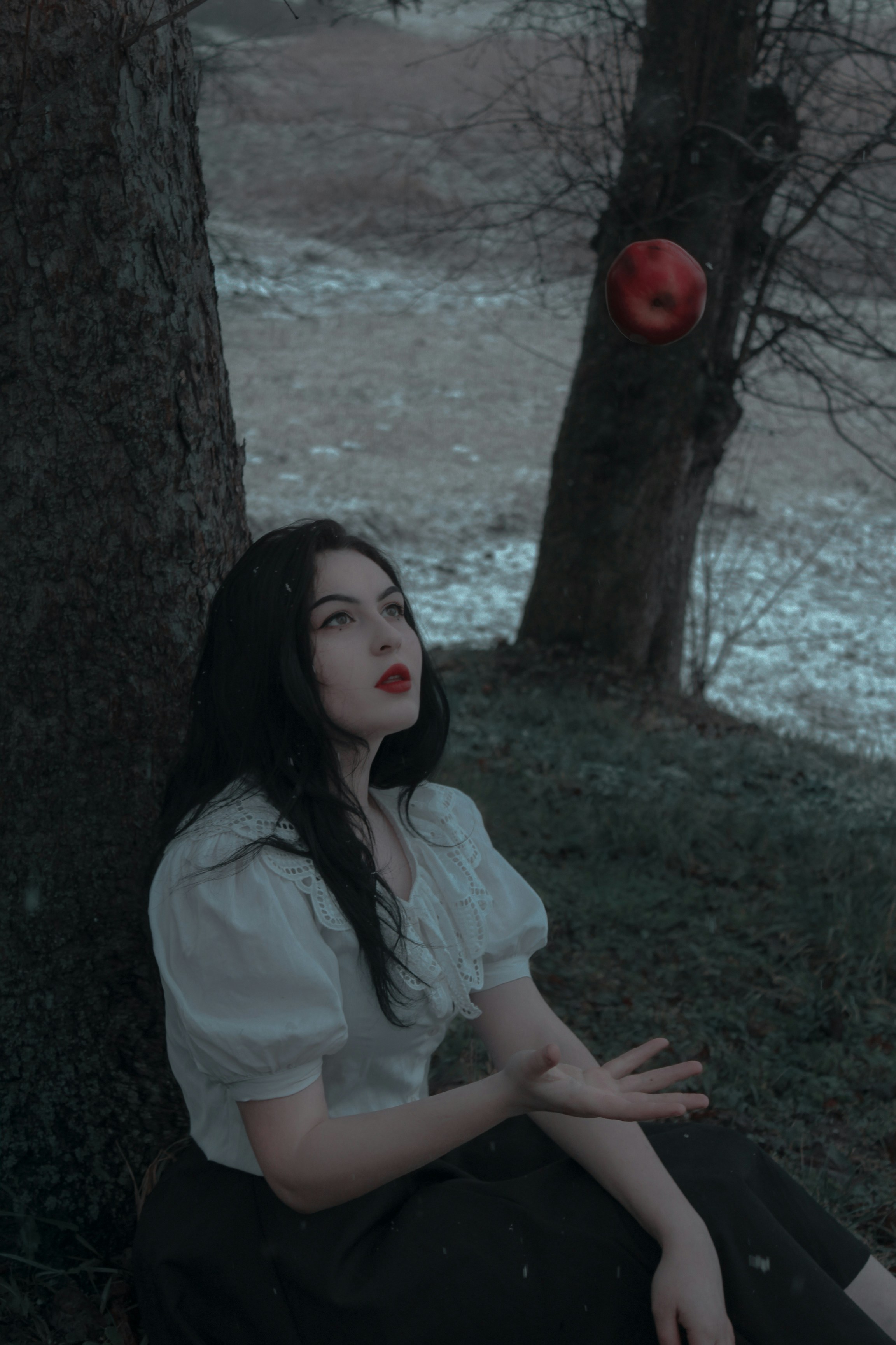 a woman sitting on the ground next to a tree