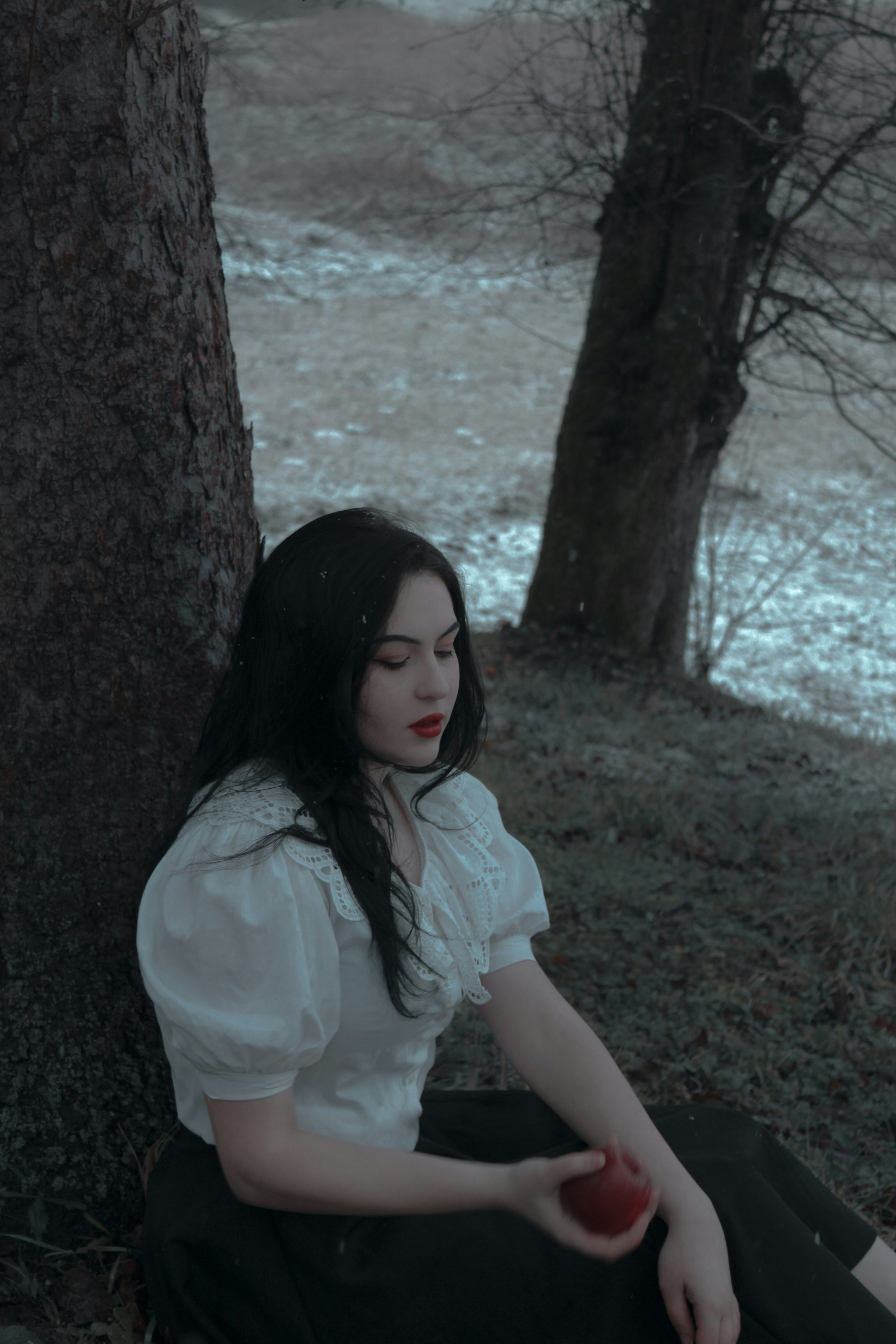 a woman sitting on the ground next to a tree