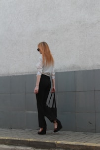 a woman walking down a sidewalk carrying a black bag