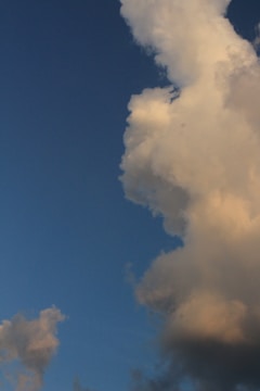 A large, fluffy cloud dominates the right side of the image against a backdrop of clear blue sky. The cloud appears illuminated by warm sunlight, creating a contrast between the vibrant sky and the soft, textured cloud.