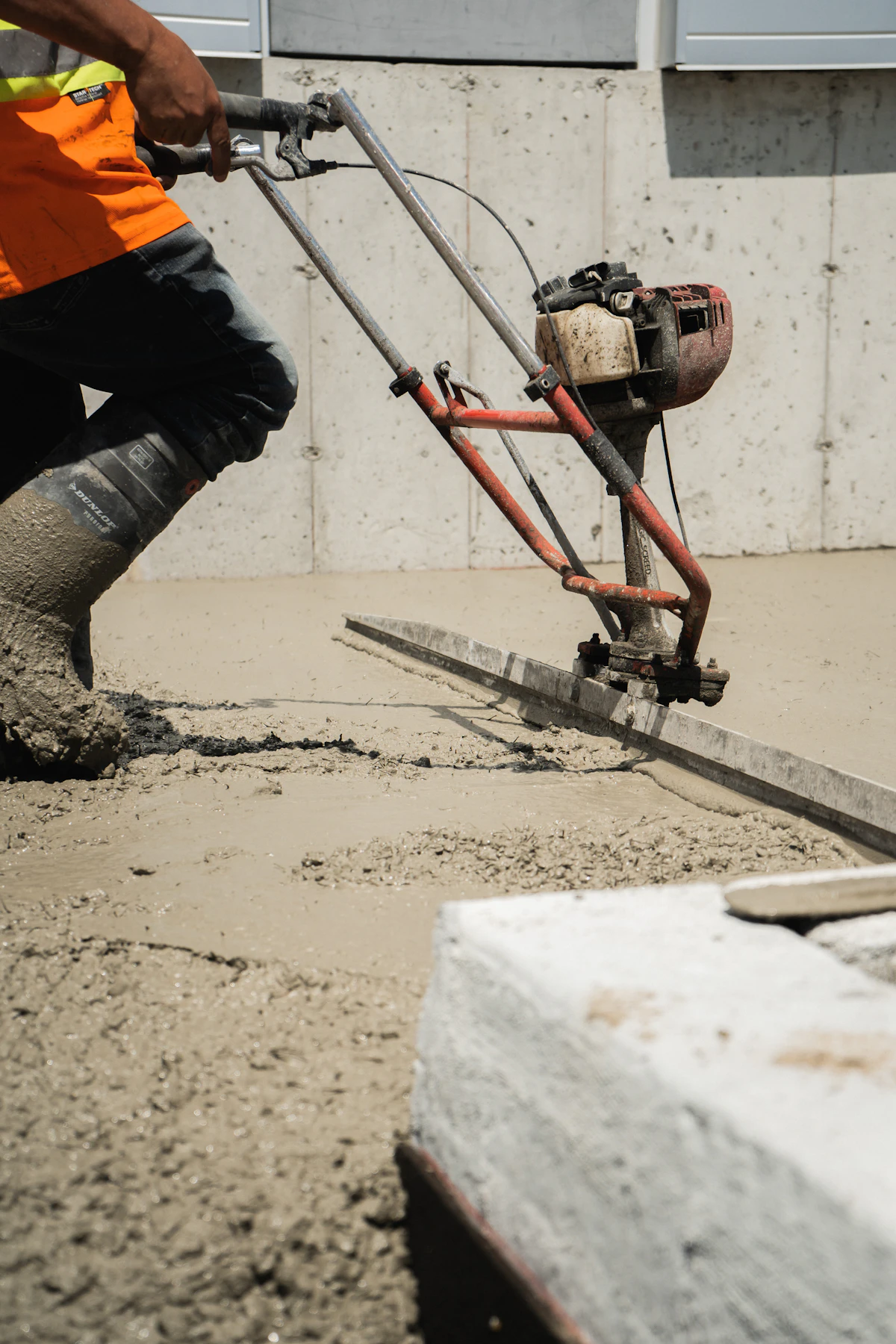 Worker running a power screed across a fresh concrete slab