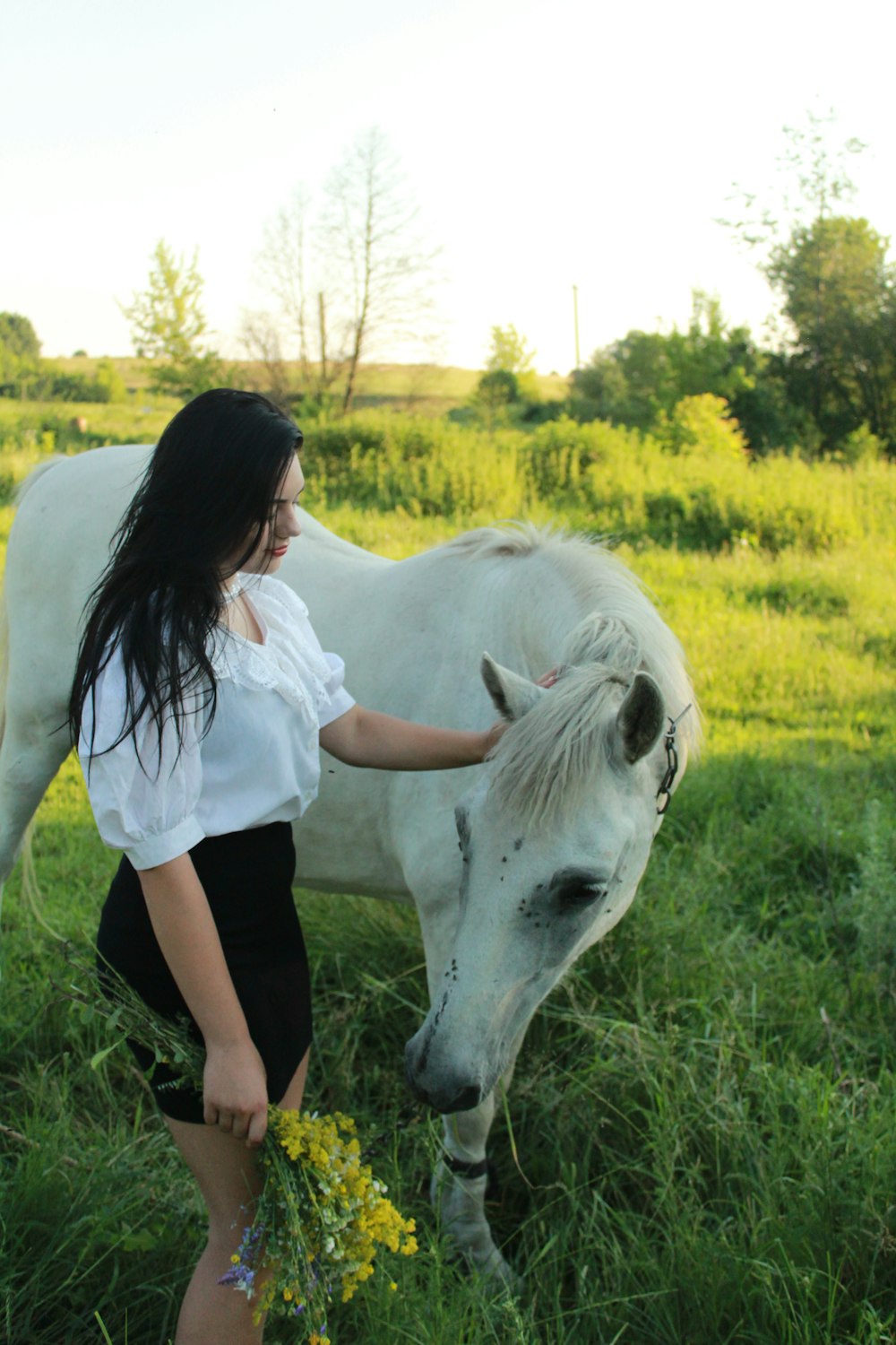 a woman standing next to a white horse on a lush green field