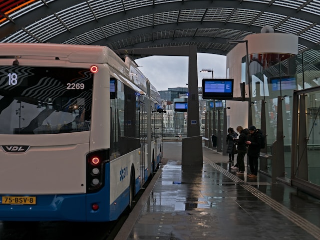 A happy traveler checking their itinerary on a smartphone while waiting at a busy bus station.