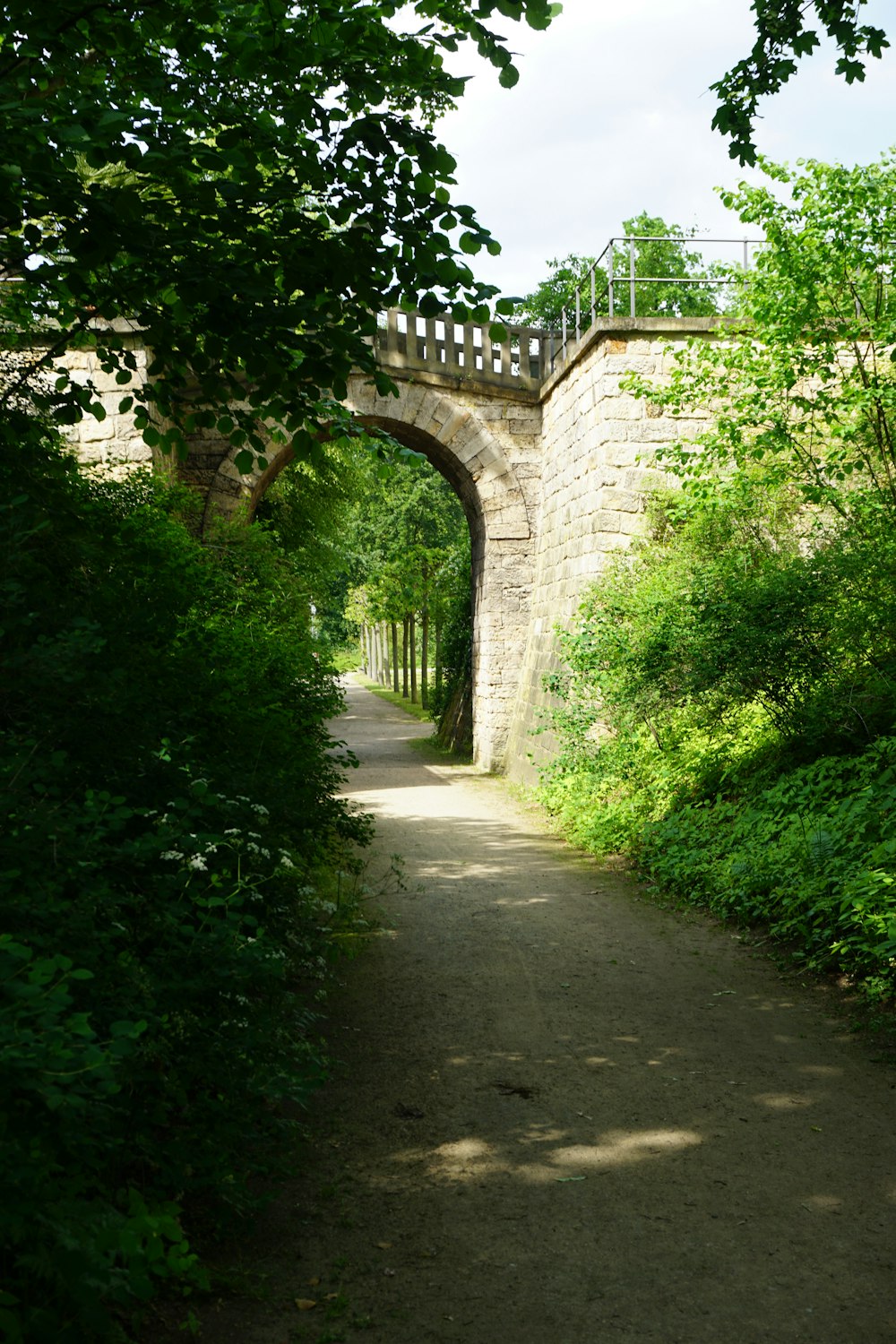 a stone bridge over a dirt road surrounded by trees