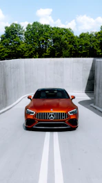 A shiny hydraulic shock absorber displayed against a backdrop of a luxury Mercedes-Benz SUV in motion on a coastal road.