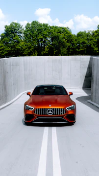 A shiny hydraulic shock absorber displayed against a backdrop of a luxury Mercedes-Benz SUV in motion on a coastal road.
