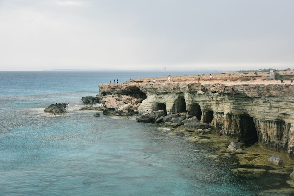 a group of people standing on top of a cliff next to the ocean