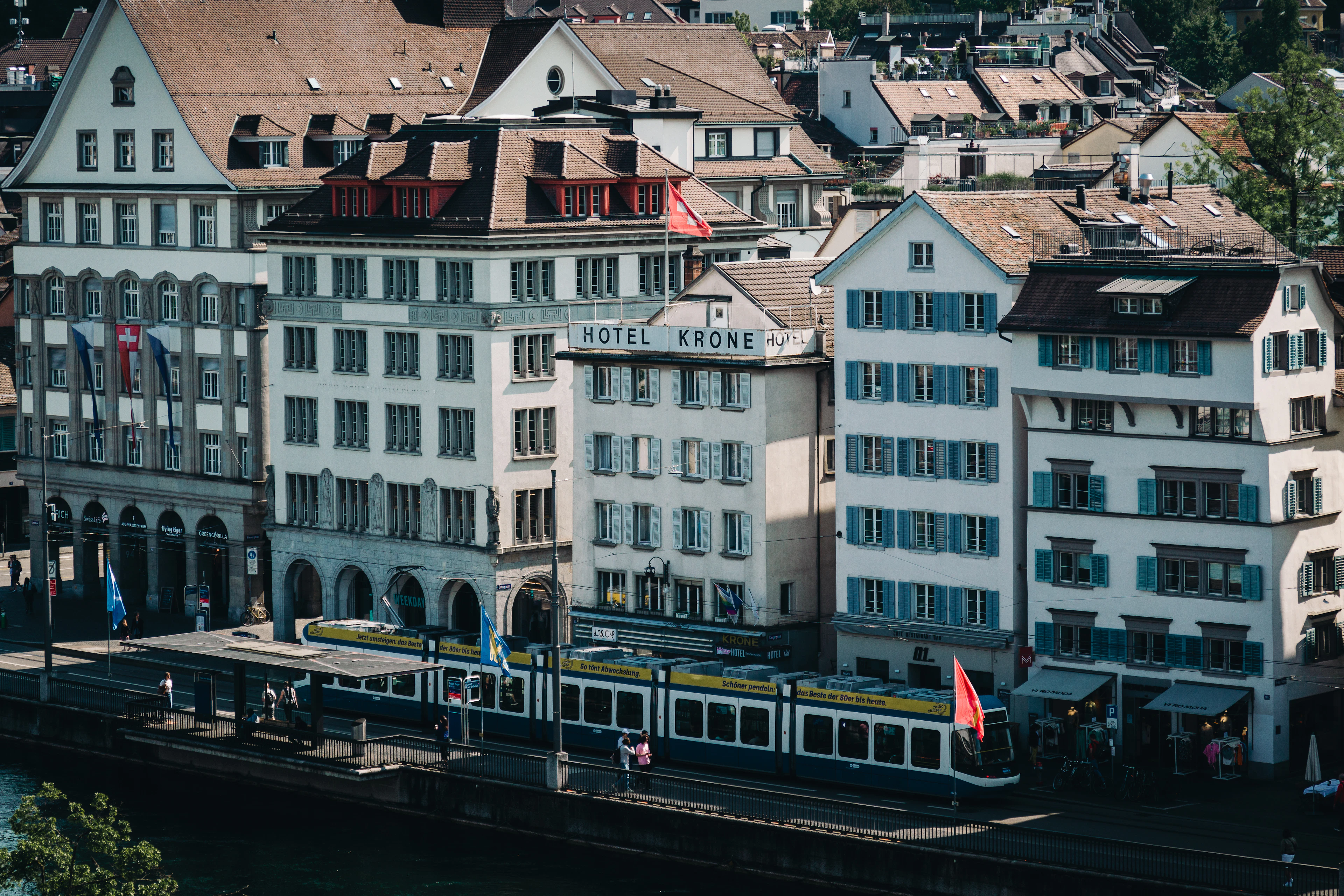 An elevated view over Zurich's old town riverside, with the white Hotel Krone building and a tram along the water.