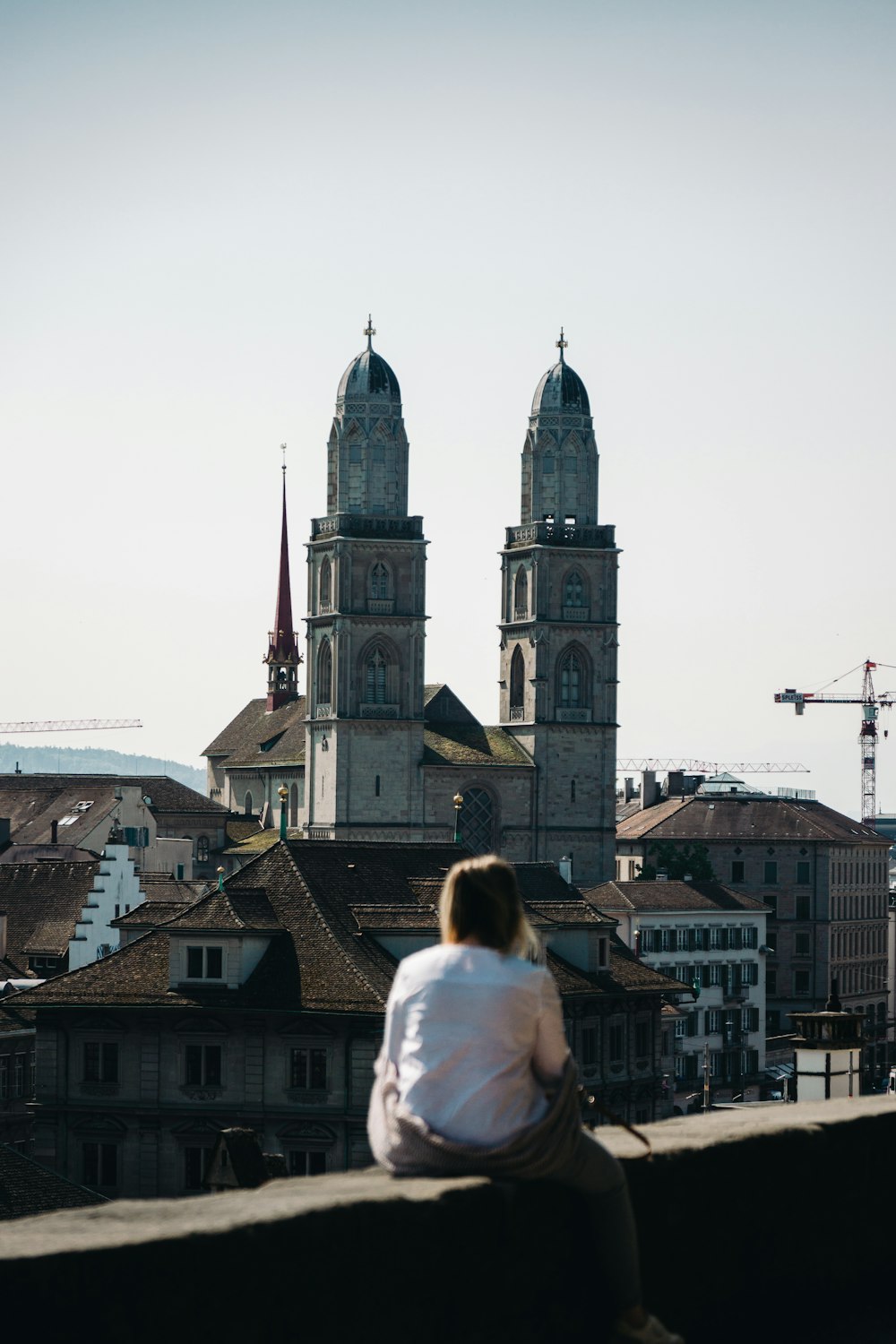 a woman sitting on a ledge looking at a city