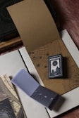 A small astrology book is placed on top of an open journal with celestial and map designs. There is also a small notepad displaying phases of the moon and a larger book with a green and gold ornate cover in the background.
