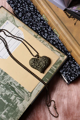 Close-up of a delicate red heart pendant resting on an open book page, symbolizing love and stories intertwined.