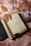 An open journal with handwritten text, surrounded by dried leaves, an old rolled parchment, a pair of reading glasses, a deck of playing cards, and a closed book with a decorative cover, all laid on a soft pink textured surface.