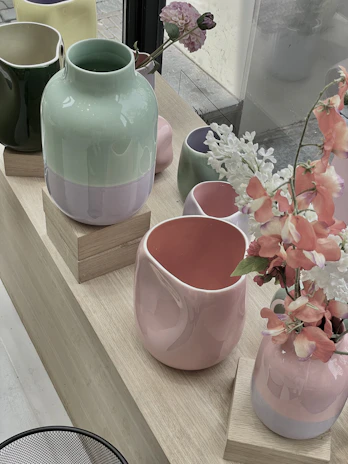 A joyful arrangement of ceramic vases in various shapes and bright pastel colors on a windowsill.
