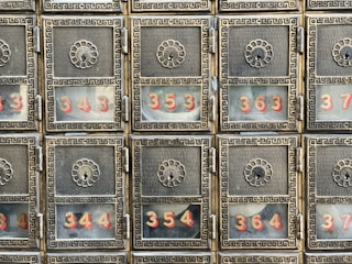A grid of six ornate metallic post office boxes with decorative floral designs around the keyholes. Each box has a glass window displaying numbers in red, such as 343, 344, 354, 363, and 364.