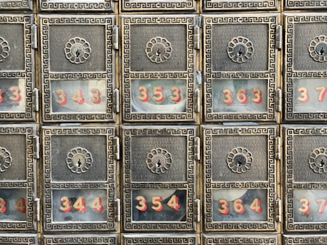 A grid of six ornate metallic post office boxes with decorative floral designs around the keyholes. Each box has a glass window displaying numbers in red, such as 343, 344, 354, 363, and 364.
