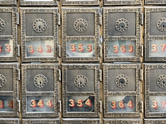 A grid of six ornate metallic post office boxes with decorative floral designs around the keyholes. Each box has a glass window displaying numbers in red, such as 343, 344, 354, 363, and 364.