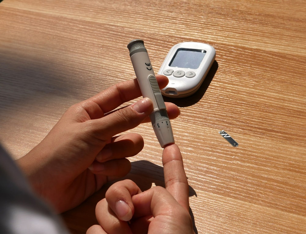 a person holding a pen and a cell phone on a table