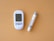 A blood glucose meter displaying a reading of 103 mg/dL is next to a lancing device on a solid light brown background. The meter and device are white with grey accents.