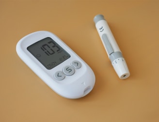 A white digital blood glucose meter displaying a reading of 103 mg/dL is placed next to a white lancet device on a light brown surface.