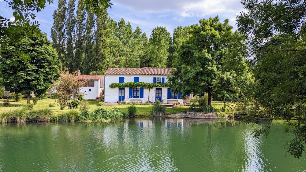 a house sitting on the side of a river next to a lush green forest