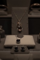 A display of elegant jewelry including a central necklace with a large gemstone, earrings, and other jewels arranged on a soft, neutral-colored surface under soft lighting.