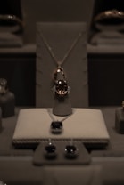 A display of elegant jewelry including a central necklace with a large gemstone, earrings, and other jewels arranged on a soft, neutral-colored surface under soft lighting.