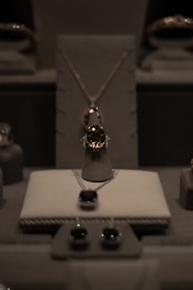 A display of elegant jewelry including a central necklace with a large gemstone, earrings, and other jewels arranged on a soft, neutral-colored surface under soft lighting.