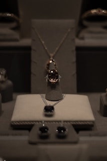 A display of elegant jewelry including a central necklace with a large gemstone, earrings, and other jewels arranged on a soft, neutral-colored surface under soft lighting.