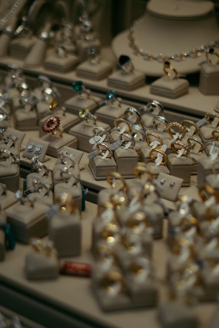 Various pieces of jewelry including rings and earrings are elegantly displayed on cushion mounts. The arrangement showcases the intricate design and sparkle of each item, with gold and silver tones standing out among gemstones of different colors.
