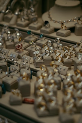 Various pieces of jewelry including rings and earrings are elegantly displayed on cushion mounts. The arrangement showcases the intricate design and sparkle of each item, with gold and silver tones standing out among gemstones of different colors.