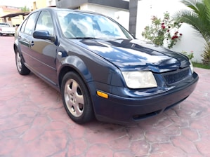 Shiny, freshly washed blue sedan parked outside a cozy home driveway on a sunny day.
