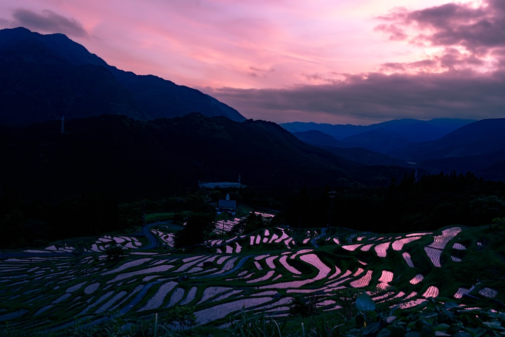 a sunset view of a valley with mountains in the background