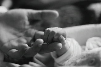 Close-up photo of a baby's hand gently holding a mother’s finger, symbolizing connection.