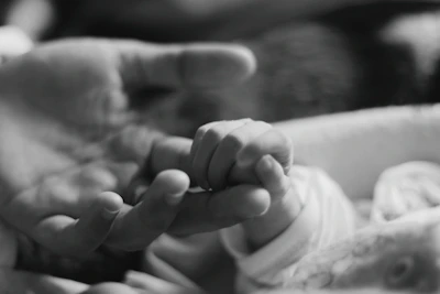 Close-up photo of a baby's hand gently holding a mother’s finger, symbolizing connection.