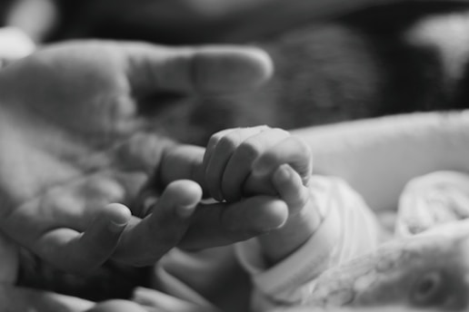 a black and white photo of a person holding a baby's hand