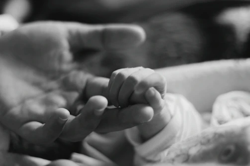 Close-up of delicate baby hand resting on mother's finger, symbolizing connection