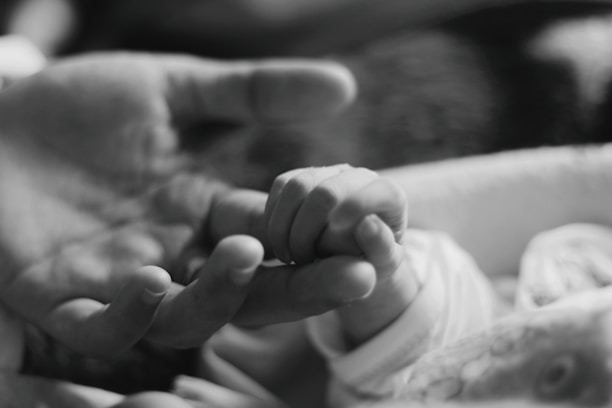 Close-up of a baby's hand gently grasping an adult's finger, symbolizing care and connection.