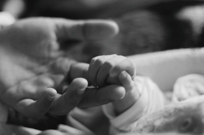 a black and white photo of a person holding a baby's hand