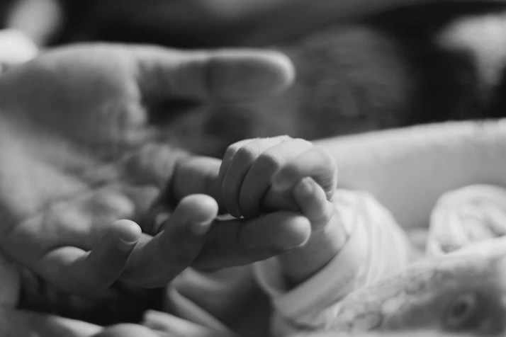 a black and white photo of a person holding a baby's hand