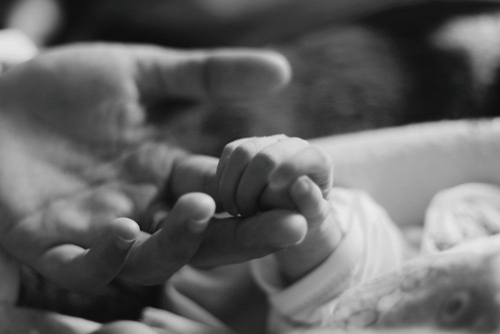 a black and white photo of a person holding a baby's hand