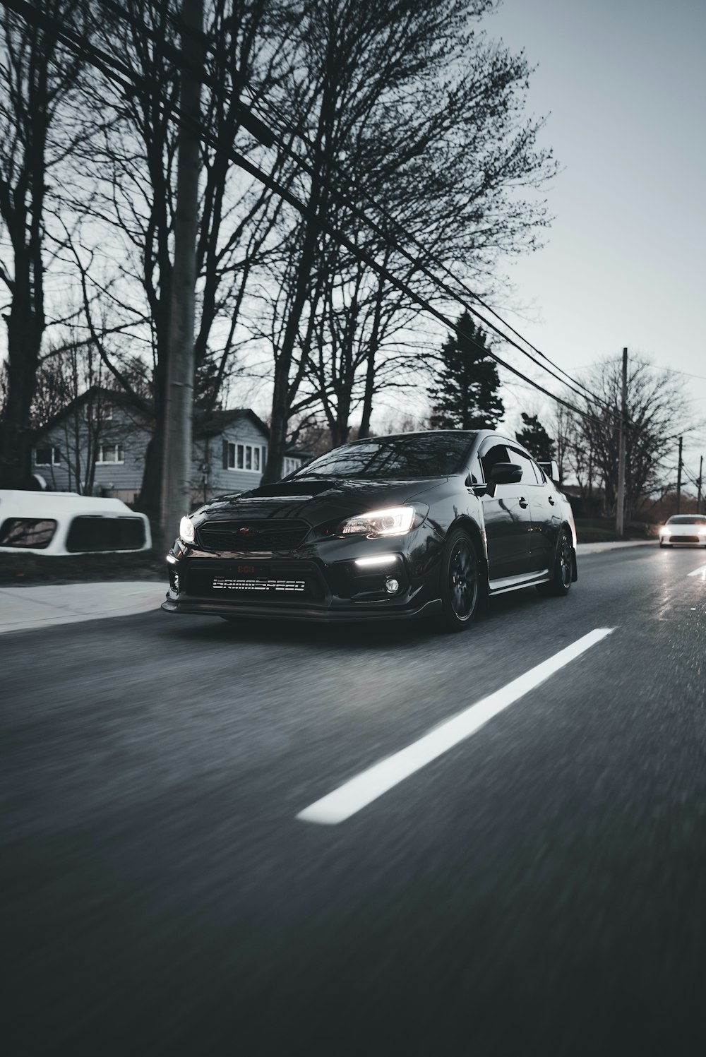 a black car driving down a street next to trees