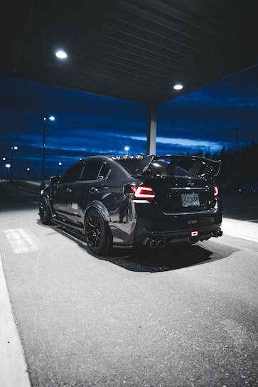 A sleek black car being loaded onto a dark trailer under a night sky.