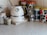 A kitchen countertop features a white electric kettle with a silver band and a temperature gauge. Next to it, there are several colorful patterned storage canisters with retro designs in green, blue, and red. A ceramic container holds kitchen utensils like a whisk and measuring spoons. The background consists of light beige tiled walls.