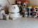 A kitchen countertop features a white electric kettle with a silver band and a temperature gauge. Next to it, there are several colorful patterned storage canisters with retro designs in green, blue, and red. A ceramic container holds kitchen utensils like a whisk and measuring spoons. The background consists of light beige tiled walls.