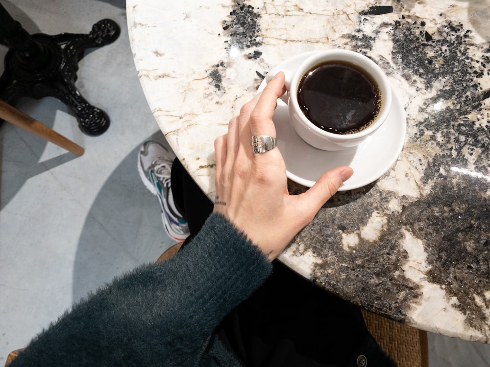 a person holding a cup of coffee on a marble table