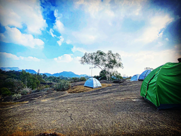 A compact toilet tent set up on rocky terrain with mountains in the background.