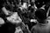 A group of people are gathered closely around a person handing out newspapers. The scene is busy, with everyone focused on receiving the papers. The lighting is dramatic, highlighting the expressions on people's faces.