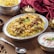 A plate of biryani garnished with mint leaves, cashews, and pieces of meat. The dish is served on an ornate silver platter, surrounded by decorative elements including a red cloth and candle holders. A serving of raita in a small bowl and a silver spoon are placed nearby.