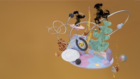 A surreal arrangement of abstract shapes, including loops, spirals, and floating spheres, all displayed on a colorful platform with a wavy, pastel design. Various textures are present, such as smooth, metallic, and feathery forms, creating a dynamic and visually engaging composition.